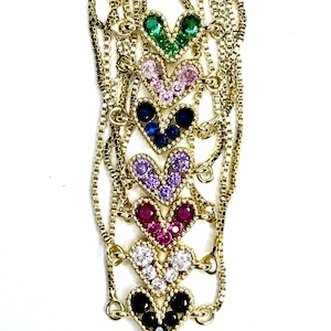 May include: Gold-toned necklaces with heart-shaped pendants. Each heart is encrusted with colorful gemstones, including green, pink, blue, purple, red, white, and black. The chains have a delicate, box-link design, and the pendants are arranged vertically.