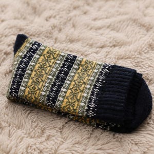 Peut inclure: Une chaussette en tricot avec un motif Fair Isle multicolore en bleu marine, vert olive, jaune moutarde et blanc. La chaussette présente un revers côtelé bleu marine uni et une pointe assortie de couleur bleu marine, avec un motif géométrique.