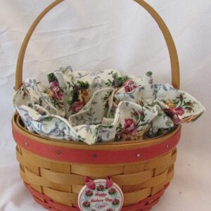 May include: A woven basket with a wooden handle and a red rim. The basket is lined with floral fabric and has a decorative tag that reads "Happy Mothers Day 1998". The basket is designed for gift giving.