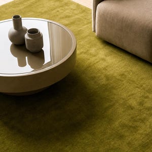Peut inclure: Scène de salon moderne avec une table basse ronde, deux vases en céramique grise et un tapis vert olive. Un coin d'un fauteuil beige est visible en arrière-plan, créant une ambiance chaleureuse.