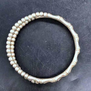 May include: Silver bracelet with a bamboo-style design. One side has a double row of small, round beads, the other a segmented bamboo pattern. The bracelet is circular and made of metal. The design is reminiscent of bamboo.