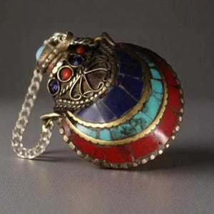 May include: A detailed pendant with a silver chain. The pendant features a crescent design with red, turquoise, and blue stone inlays. The top has a decorative silver filigree design with red and blue stones.