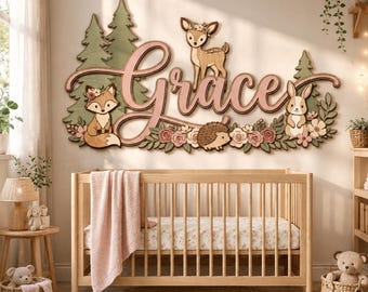 May include: A wall-mounted wooden sign featuring the name Grace in large pink script lettering, surrounded by layered cutouts of green pine trees, a fox, a deer, a hedgehog, a rabbit, and pink flowers, positioned above a wooden crib.
