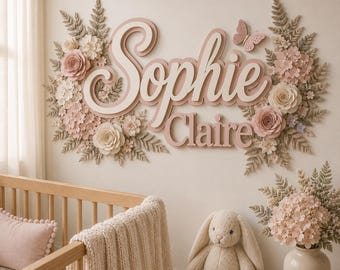 May include: A wall-mounted sign featuring the name Sophie Claire in layered pink and white script lettering, surrounded by decorative paper flowers, fern-like foliage, and a butterfly cutout, displayed above a wooden crib and a plush toy.