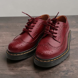May include: A pair of burgundy leather brogue shoes with a thick black sole and yellow stitching. The shoes have a classic lace-up design with decorative perforations and a rounded toe.