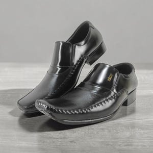 May include: Pair of black leather slip-on dress shoes. The shoes have a textured vamp and a stitched design along the edges. The shoes are displayed on a gray surface.