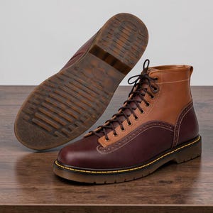 May include: Two-tone leather boots in brown and tan with a lace-up design. The boots have a sturdy sole with a yellow stitch detail and a contrasting brown sole. The second boot is displayed with the sole facing up.