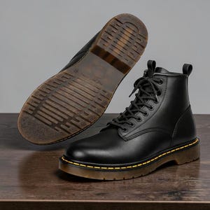 May include: Black leather ankle boots with a lace-up design and a contrasting yellow stitch detail. The boots have a brown sole and a classic, durable construction. One boot is shown from the sole, displaying the tread pattern.
