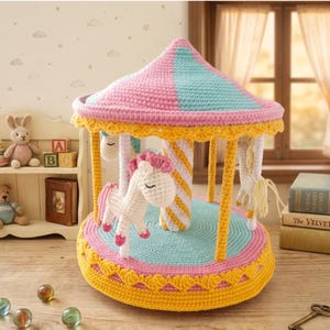 May include: A handmade crochet carousel toy in pastel colors. The carousel features a pink and blue striped roof, yellow trim, and white and pink horses. The base is light blue and yellow, with a detailed crochet design.