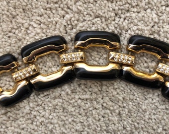 Könnte beinhalten: Ein schwarzes und goldenes Armband mit quadratischem Gliederdesign. Jedes Glied ist mit klaren Strasssteinen verziert.