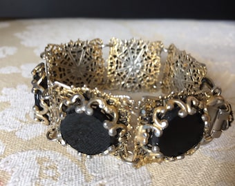 May include: A gold and silver bracelet with black glass stones. The bracelet is made of filigree metal and has a clasp closure.