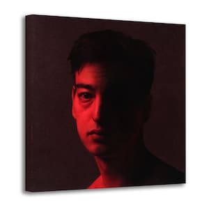 May include: A square canvas print featuring a portrait of a person with dark hair, illuminated by a deep red light. The lighting creates a high-contrast effect, casting one side of the face into shadow while highlighting the other in vibrant red.