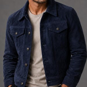 Könnte beinhalten: Eine dunkelblaue Wildlederjacke mit klassischem Kragen, langen Ärmeln und einer Knopfleiste mit passenden Knöpfen. Die Jacke verfügt über zwei Brusttaschen mit geknöpften Klappen und wird über einem schlichten hellbeigen T-Shirt und einer schwarzen Hose getragen.