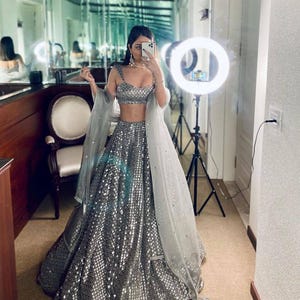 May include: A silver sequined two-piece formal dress with a matching sheer shawl. The top is a crop top with thin straps, and the skirt is a full-length A-line. The dress is worn with a necklace and earrings. The text "FB L135" is visible.