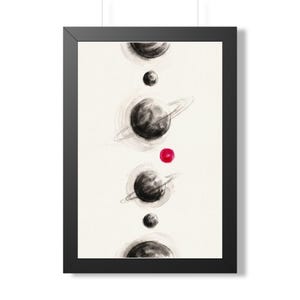 May include: A framed vertical wall art print featuring a series of celestial bodies arranged in a column. The artwork displays black ink wash planets, two of which have rings, and a single small, vibrant red circular dot on a cream background.