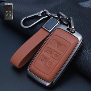 以下が含まれることがあります： メタリックフレームとタンカラーのレザーストラップが付いた、タンカラーのレザー製カーキーフォブカバー。カバーには、ハザードランプ、トランクリリース、ヘッドライト、ロックおよびアンロックのシンボルなど、車両機能を示すエンボス加工されたアイコンが施されています。
