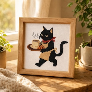 Könnte beinhalten: Ein gerahmtes Kreuzstichbild, das eine schwarze Katze mit beiger Schürze und rotem Schal zeigt. Die Katze trägt ein braunes Tablett mit einer dampfenden weißen Tasse und einem Croissant. Das Bild befindet sich in einem hellen Holzrahmen.