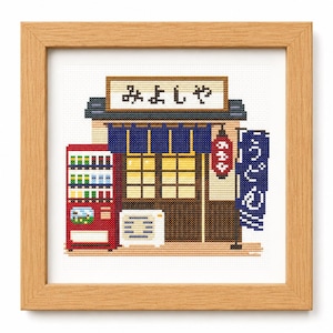 May include: A cross-stitch embroidery in a light wood frame depicting a Japanese storefront with a red vending machine, a blue noren curtain, a red lantern, and a blue banner with white text. The sign above the entrance displays the text "みよしや".