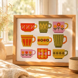 May include: A framed cross-stitch embroidery featuring a grid of nine colourful mugs. The mugs display various patterns including flowers, stripes, and geometric shapes in shades of red, orange, yellow, green, and pink on a white fabric background.