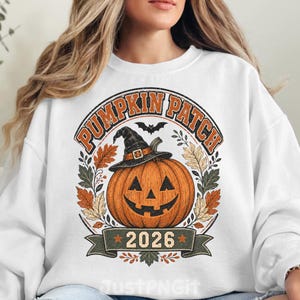 May include: A white long-sleeve sweatshirt featuring a graphic of an orange jack-o'-lantern wearing a black witch hat. The design includes the text PUMPKIN PATCH and 2026, surrounded by autumn leaves and a small black bat silhouette above the pumpkin.