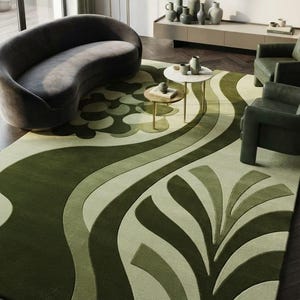 Könnte beinhalten: Ein großer rechteckiger Teppich mit einem geschichteten, abstrakten botanischen Muster in verschiedenen Grün-, Oliven- und Salbeitönen. Das Design umfasst geschwungene Linien und stilisierte Blattmotive mit einer texturierten, getufteten Oberfläche.