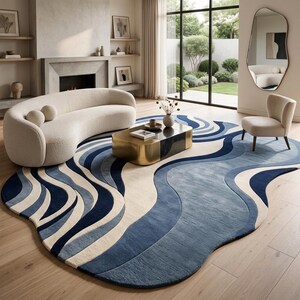 Könnte beinhalten: Ein Teppich mit unregelmäßiger, organischer Form und einem geschichteten Wellenmuster in Marineblau, Hellblau und Cremetönen. Der Teppich liegt auf einem hellen Holzboden und erstreckt sich unter einem geschwungenen cremefarbenen Sofa und einem Sessel.