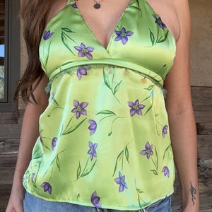 May include: A lime green halter top with a floral pattern of purple flowers and green stems. The top has a V-neck and a decorative trim along the bust line. The fabric has a slight sheen.