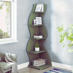 May include: Olive green corner bookshelf with a distinctive, undulating shape. The shelves display books, framed art, a small plant, and a wire basket. The bookshelf is positioned in a corner near a window and a chair.