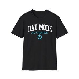 May include: Black t-shirt with the text "DAD MODE ACTIVATED" in white and light blue. A light blue power symbol is below the text. The shirt is a crew neck and has short sleeves.