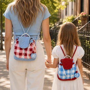 May include: Two crochet backpacks with drawstring closures and top handles. The larger bag features a red and white gingham pattern with a blue flap and base. The smaller bag has a blue and white gingham pattern with a red flap and base.
