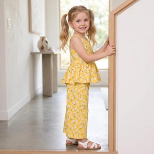 Op de afbeelding: Een tweedelige outfit bestaande uit een mouwloze peplumtop en een bijpassende broek met wijde pijpen, beide met een felgele achtergrond en een herhalend patroon van kleine witte madeliefjes met gele hartjes, gecombineerd met witte sandalen.