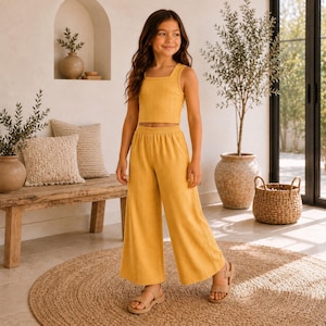 May include: A mustard yellow two-piece set consisting of a sleeveless ribbed crop top with a square neckline and matching wide-leg trousers. The outfit is made of a textured fabric and is paired with simple beige strappy sandals.