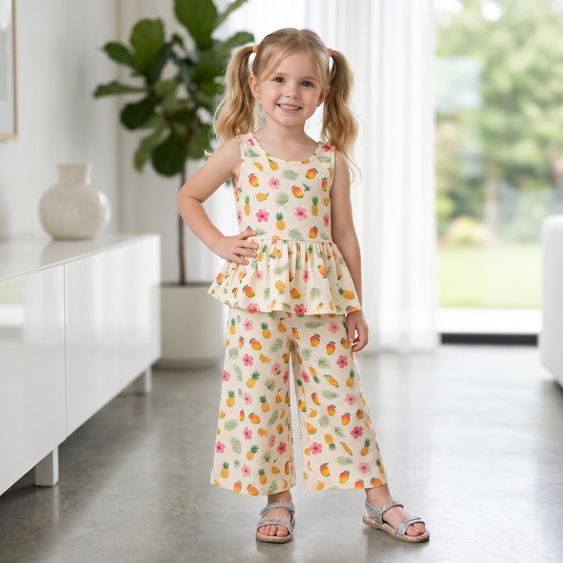 Op de afbeelding: Een tweedelige set bestaande uit een mouwloze peplumtop en een wijde broek, beide voorzien van een all-over print van gele ananassen, oranje mango's, roze hibiscusbloemen en groene palmbladeren op een cr&egrave;mekleurige achtergrond.
