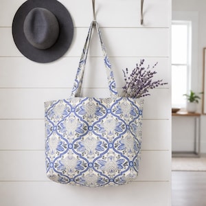 May include: A tote bag with a blue and white floral pattern hangs on a wall. The bag is filled with lavender. A gray fedora hat hangs on the wall to the left of the bag.