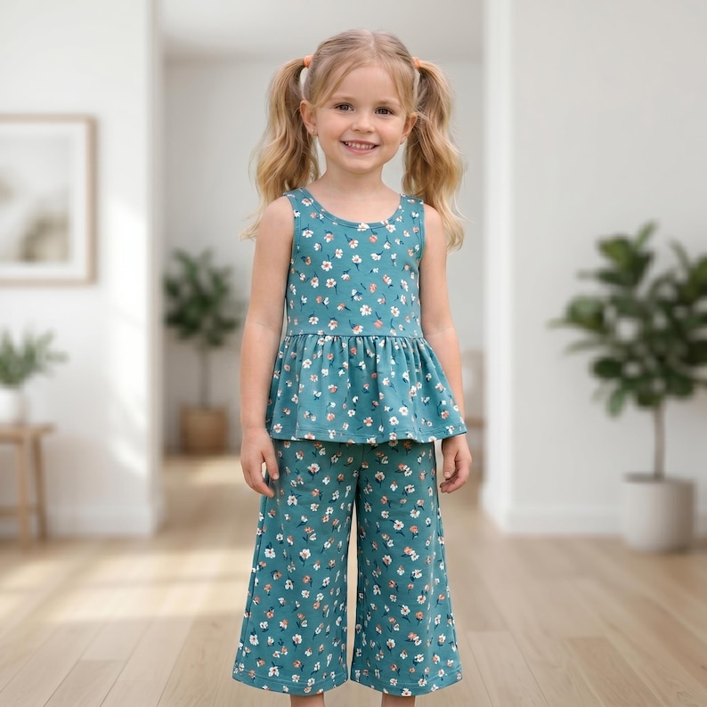 Op de afbeelding: Een set bestaande uit een mouwloze peplumtop en een bijpassende wijde, kortere broek in een blauwgroene kleur, voorzien van een herhalend patroon van kleine witte en oranje bloemen met groene blaadjes. De set heeft een ronde halslijn.
