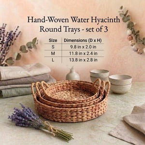 Puede incluir: Juego de tres bandejas redondas de jacinto de agua tejidas a mano. Las bandejas tienen una textura tejida natural e incluyen tamaños con dimensiones de 25 cm x 5 cm, 30 cm x 6 cm y 35 cm x 7 cm. La imagen también muestra lavanda y lino.