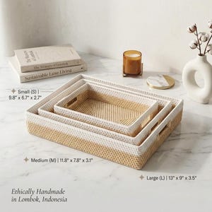 May include: A set of three rectangular woven storage trays in varying sizes. The trays are two-toned, with a natural beige base and a white upper section. The dimensions are: Small (9.8" x 6.7" x 2.7"), Medium (11.8" x 7.8" x 3.1"), and Large (13" x 9" x 3.5"). The text reads "Ethically Handmade in Lombok, Indonesia."