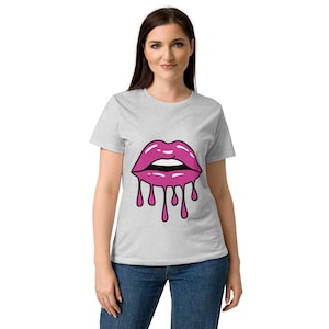 May include: A light gray t-shirt featuring a graphic of pink lips with dripping paint. The lips are outlined in black and have a glossy finish. The shirt is a short-sleeved crew neck.