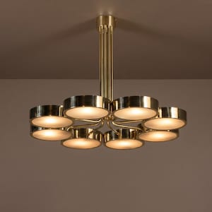 Peut inclure: Un lustre moderne en laiton, composé de huit luminaires circulaires. Les lumières sont disposées en cercle, avec une tige centrale et une lueur chaleureuse et accueillante. Le luminaire est fixé au plafond de couleur neutre.