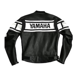 Puede incluir: Una chaqueta de moto de cuero negro con rayas horizontales blancas en la espalda y los hombros. La palabra YAMAHA está impresa en letras mayúsculas negras sobre una banda horizontal blanca en la parte superior de la espalda.