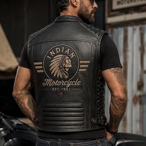 Puede incluir: Un chaleco de moto de cuero negro con un gran parche circular en la espalda con el texto Indian Motorcycle Est. 1901 y una ilustración de una persona con un tocado. El chaleco tiene cordones laterales y un acolchado horizontal en la base.