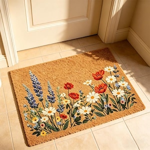 Può includere: Un zerbino rettangolare in fibre naturali, con un motivo floreale. I fiori includono papaveri rossi, margherite bianche e lavanda blu. Il tappeto è posto davanti a una porta bianca su un pavimento piastrellato.