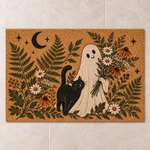 May include: A rectangular tan doormat featuring a black cat standing next to a white ghost holding a bouquet of wildflowers. The design includes green fern fronds, white daisies, orange flowers, and a black crescent moon with small stars.