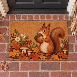 May include: A rectangular coir doormat featuring a printed illustration of a brown squirrel holding an acorn. The scene includes orange and yellow autumn leaves, white daisy flowers, red berries, and two brown mushrooms on a tan background.