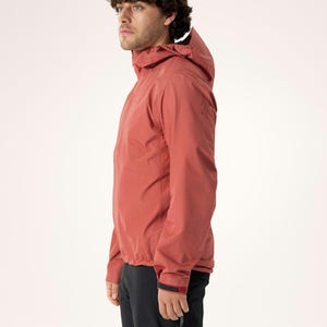 Puede incluir: Chaqueta con capucha de color &oacute;xido con cierre de cremallera. La chaqueta tiene un dise&ntilde;o estilizado y se combina con pantalones negros. El modelo est&aacute; mirando hacia la izquierda, mostrando el perfil lateral de la chaqueta. La chaqueta parece estar hecha de un material ligero y resistente al agua.