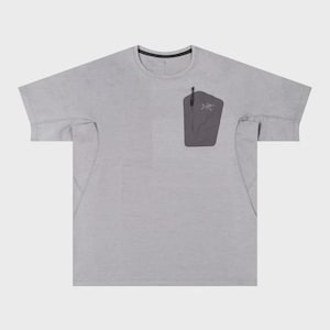 May include: A light gray t-shirt with a crew neck and short sleeves. It features a dark gray pocket on the chest with a zipper and a small logo. The shirt has a minimalist design.