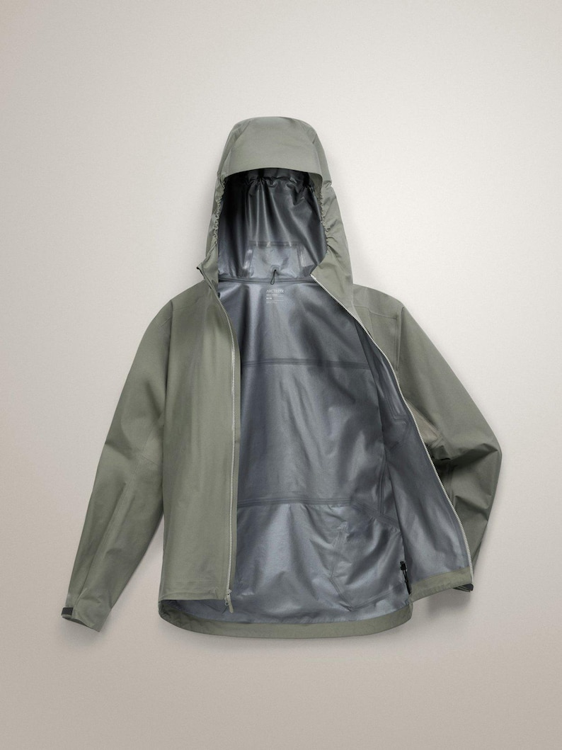 Puede incluir: Chaqueta con capucha verde salvia con cremallera completa. La chaqueta est&aacute; abierta, revelando un forro interior plateado. La capucha est&aacute; levantada y las mangas extendidas. Esta chaqueta impermeable est&aacute; dise&ntilde;ada para actividades al aire libre.