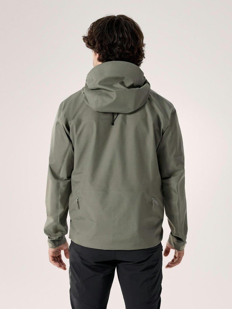 Puede incluir: Chaqueta con capucha verde salvia con cuello alto y cord&oacute;n. La chaqueta tiene dos bolsillos con cremallera y mangas largas. El modelo lleva pantalones negros. La chaqueta est&aacute; dise&ntilde;ada para actividades al aire libre.