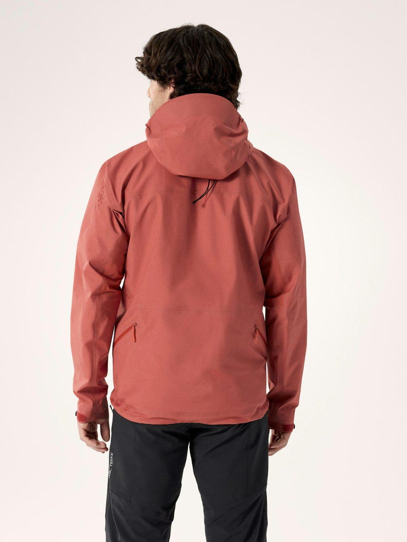 Puede incluir: Chaqueta con capucha de color &oacute;xido con cuello alto y bolsillo delantero. La chaqueta tiene mangas largas y una capucha con cord&oacute;n. La persona de la imagen lleva pantalones negros. La chaqueta est&aacute; hecha de un material duradero y resistente a la intemperie.