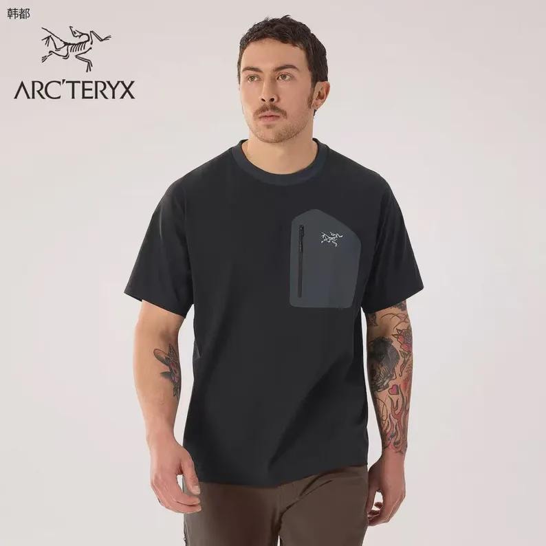 May include: Black short-sleeve t-shirt with a dark gray pocket on the chest. The pocket has a zipper and a small logo. The shirt has a crew neck and the brand name "ARC'TERYX" is printed on the upper left.